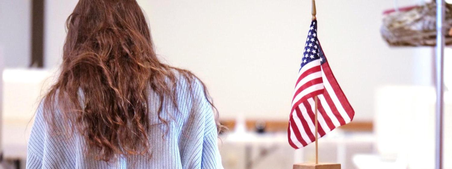 person standing next to a vote dropbox with an American flag